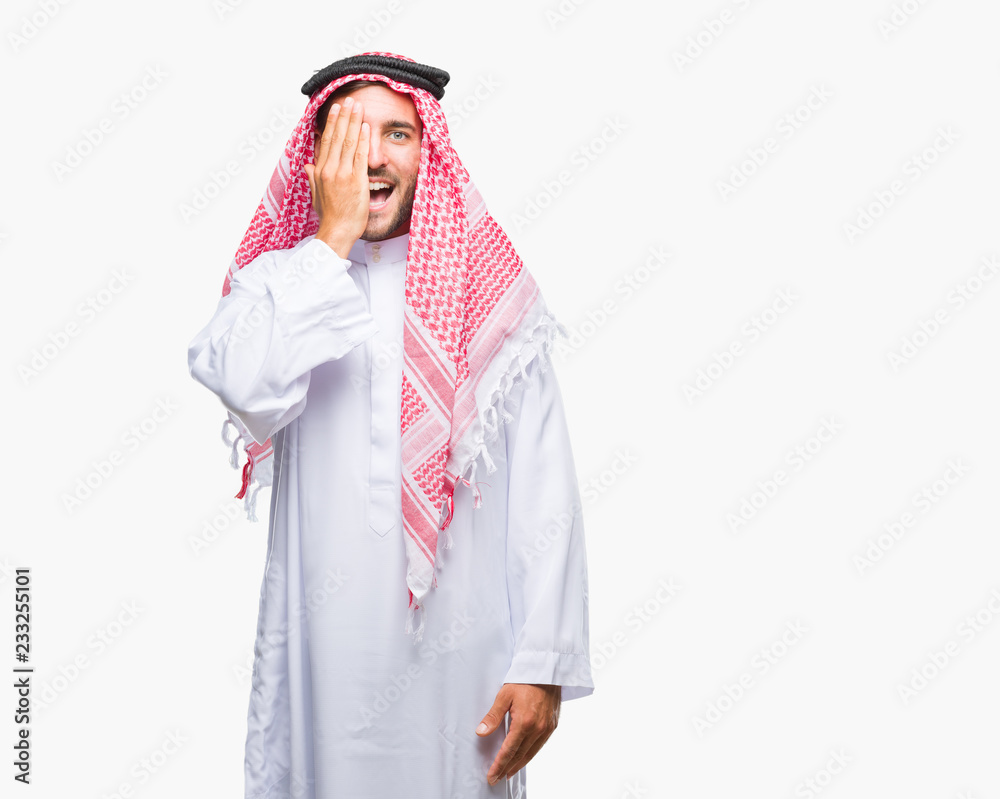 Young handsome man wearing keffiyeh over isolated background covering one eye with hand with confident smile on face and surprise emotion.