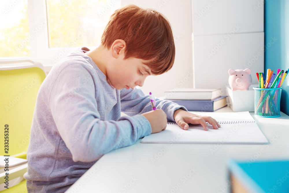nine years old child writing at home. Boy studying at table on blue background. Kid drawing with a pencil nine years old child writing at home. Boy studying at table on blue background. Kid drawing with a pencil