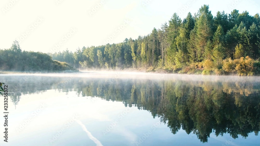 Fototapeta premium Mist over the river. Autumn forest is reflected in the water on the riverbank.