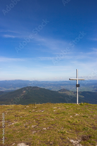 Cross on the top of mountains. Faith and memory sign. Cross standing against beautiful mountain landscape and blue sky. Vastness and peace concept. Christian religion symbol.