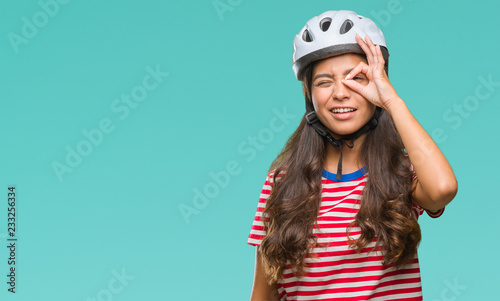 Young arab cyclist woman wearing safety helmet over isolated background doing ok gesture with hand smiling, eye looking through fingers with happy face.