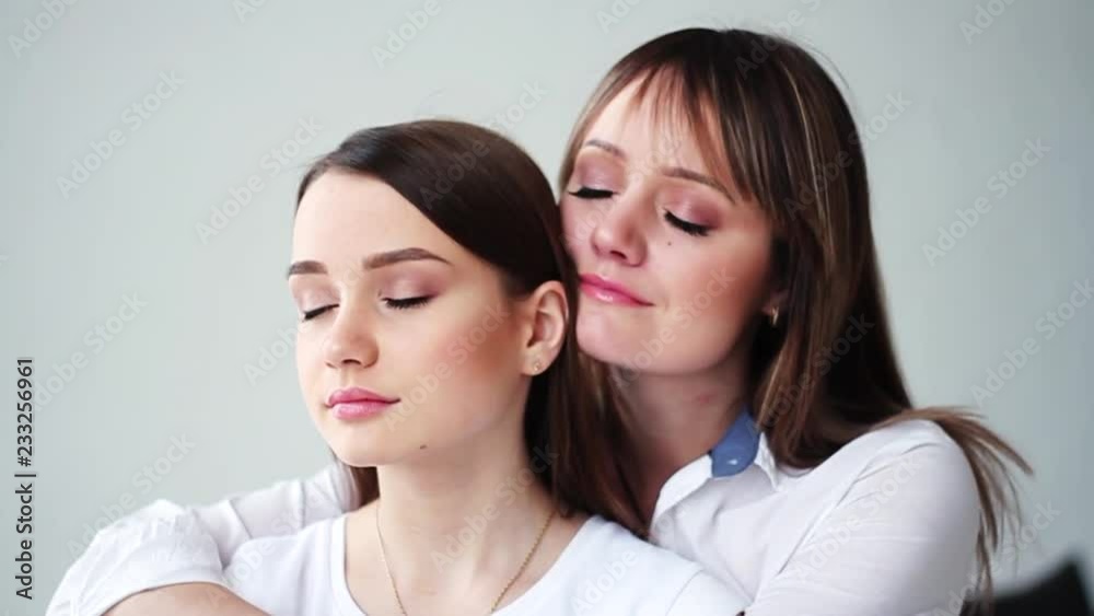 Face beautiful young mother with her daughter stand hug closed eyes smile happy in studio white background attractive family female conversation cute girl close up portrait slow motion Face beautiful young mother with her daughter stand hug closed eyes smile happy in studio white background attractive family female conversation cute girl close up portrait slow motion