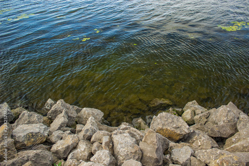 rock stones and colorful reservoir water background surface with small waves from above