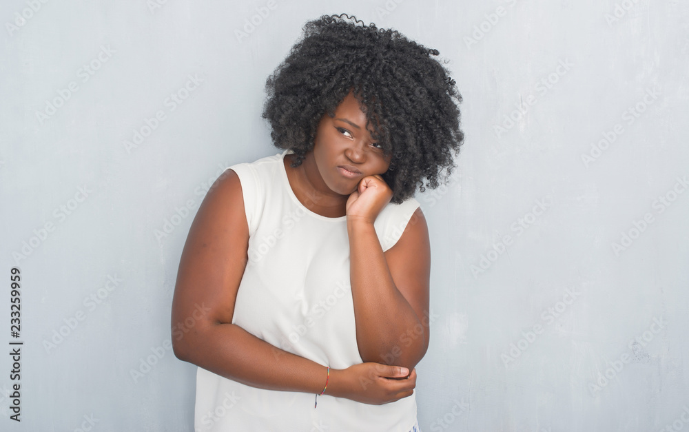 Young african american woman over grey grunge wall thinking looking tired and bored with depression problems with crossed arms. Young african american woman over grey grunge wall thinking looking tired and bored with depression problems with crossed arms.