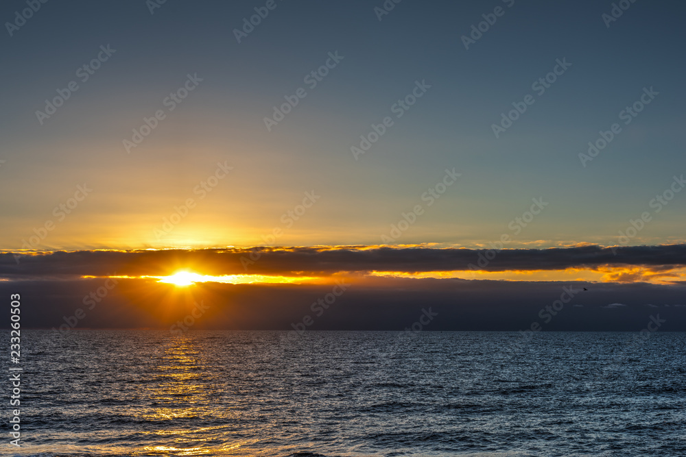 Sun shining through dark clouds over the sea at sunset