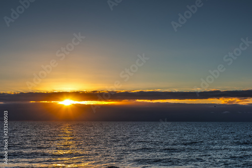 Sun shining through dark clouds over the sea at sunset