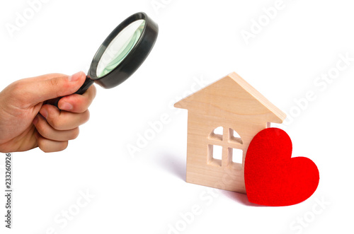 Magnifying glass is looking at the Wooden house with a red heart on a white background. Affordable housing. Family psychology. Love nest, love relationships. Buying a house with a young family.