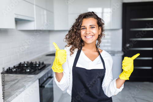 Smiling young latin cleaning lady with pink rubber gloves showing ok sign with thumbs up in the kitchen