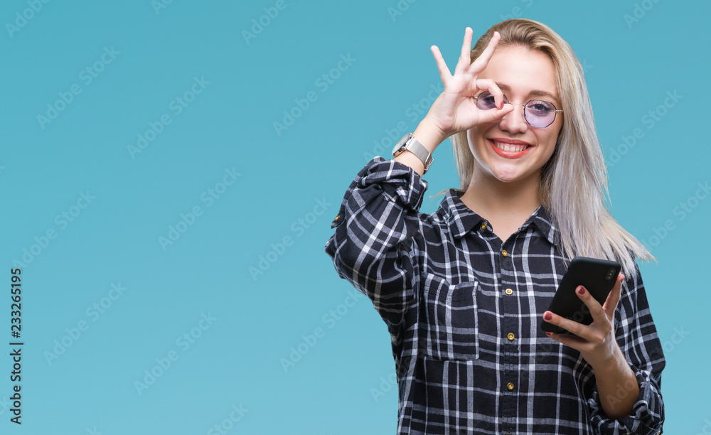 Obraz premium Young blonde woman texting sending message using smartphone over isolated background with happy face smiling doing ok sign with hand on eye looking through fingers