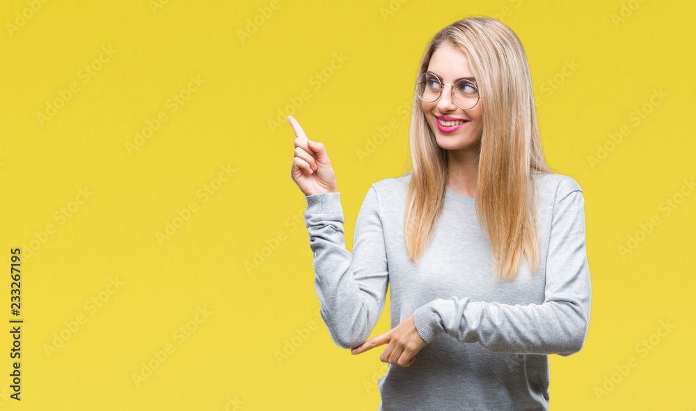 Obraz premium Young beautiful blonde woman wearing glasses over isolated background with a big smile on face, pointing with hand and finger to the side looking at the camera.