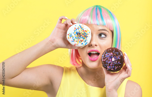 Beautiful woman in a colorful wig with doughnuts on a yellow background