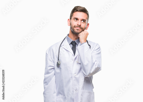 Young handsome doctor man over isolated background with hand on chin thinking about question, pensive expression. Smiling with thoughtful face. Doubt concept. © Krakenimages.com