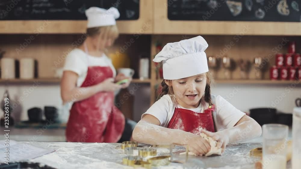 Little Cute Girl Is Cooking On Cozy Kitchen. Having Fun While Making Cakes and Cookies. Her mother is in the background Little Cute Girl Is Cooking On Cozy Kitchen. Having Fun While Making Cakes and Cookies. Her mother is in the background