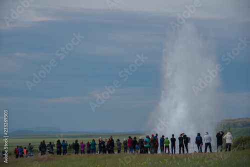 A geysir erupts in the Geysir Geothermal Area in South Iceland as a crowd watches from a distance