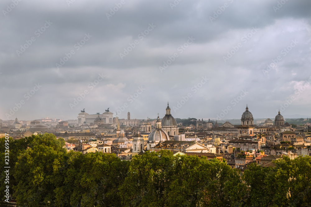 Roofs of Rome with cupolas of ancient churches and altare della Patria in the distance. Shot on a rainy day with stormy clouds and mist