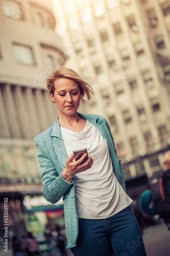 Stylish mid-age business woman texting on the street