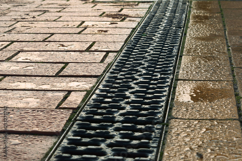 Sidewalk drainage. Grate - rain gutter on the sidewalk. Pathway paved with red and yellow tiles.
