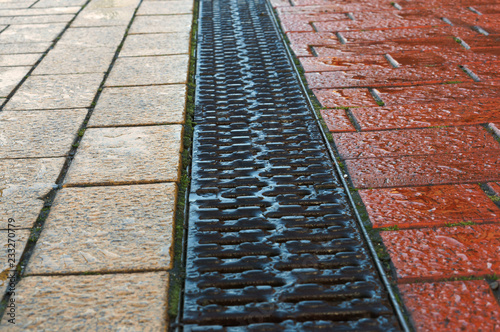 Sidewalk drainage. Grate - rain gutter on the sidewalk. Pathway paved with red and yellow tiles.