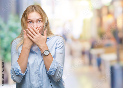 Young caucasian business woman wearing call center headset over isolated background shocked covering mouth with hands for mistake. Secret concept.