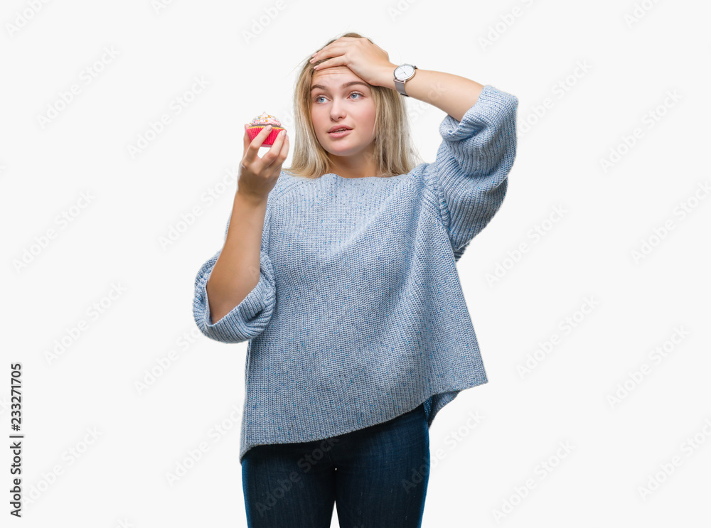 Fototapeta premium Young caucasian woman eating sweet cupcake over isolated background stressed with hand on head, shocked with shame and surprise face, angry and frustrated. Fear and upset for mistake.