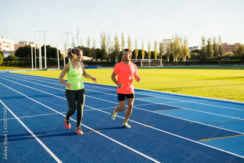 Couple of athletic runners running on a blue race track. Sport.