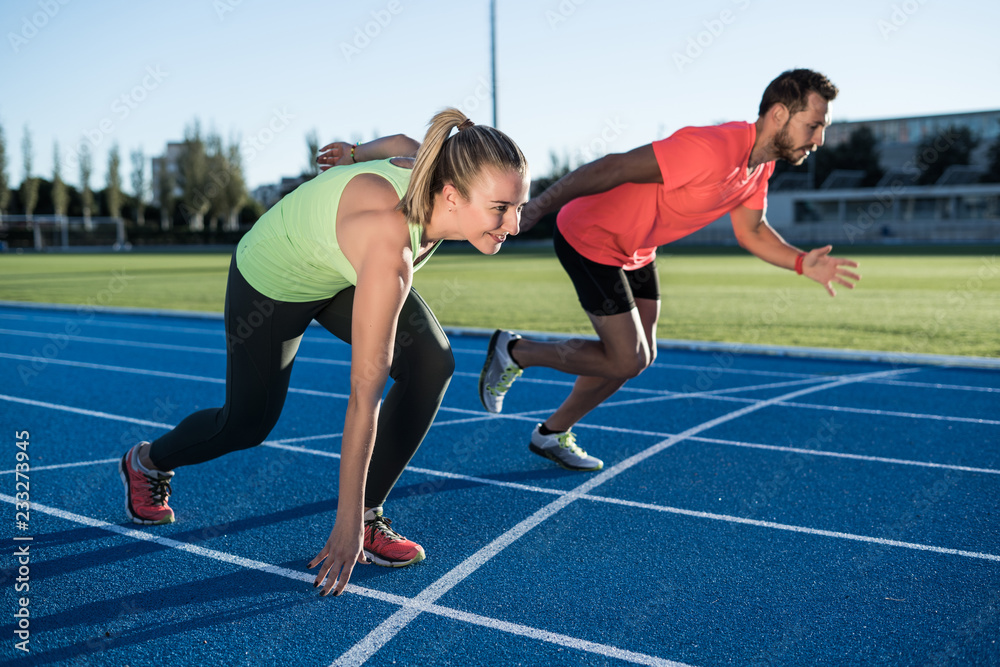 Athlete couple at starting position ready to start a race. Sprinters ready for race on race track. Woman against man.