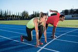 Athlete couple at starting position ready to start a race. Sprinters ready for race on race track. Woman against man.