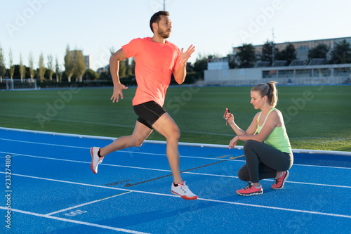 Woman is timing to runner with chronometer at the end of run in a race track. Competition.