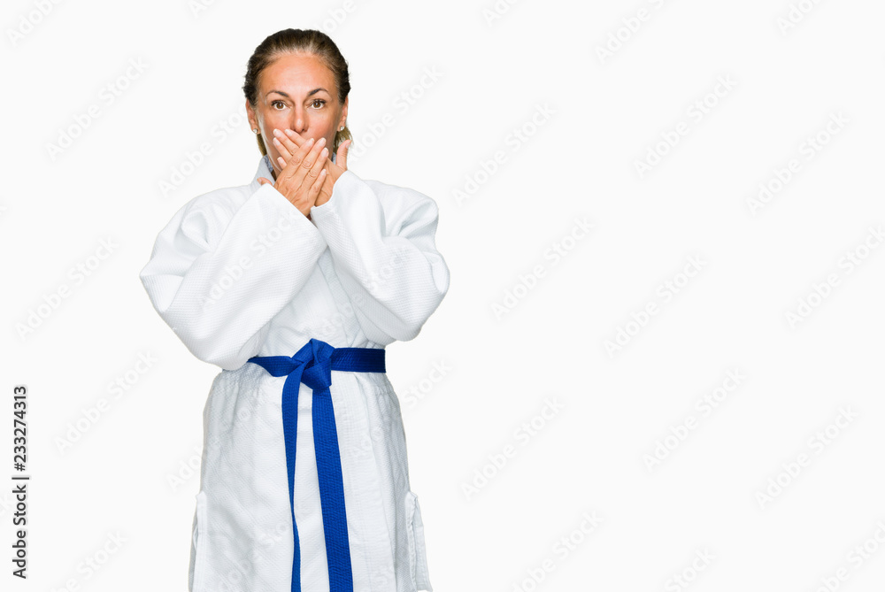 Middle age adult woman wearing karate kimono uniform over isolated background shocked covering mouth with hands for mistake. Secret concept. Middle age adult woman wearing karate kimono uniform over isolated background shocked covering mouth with hands for mistake. Secret concept.