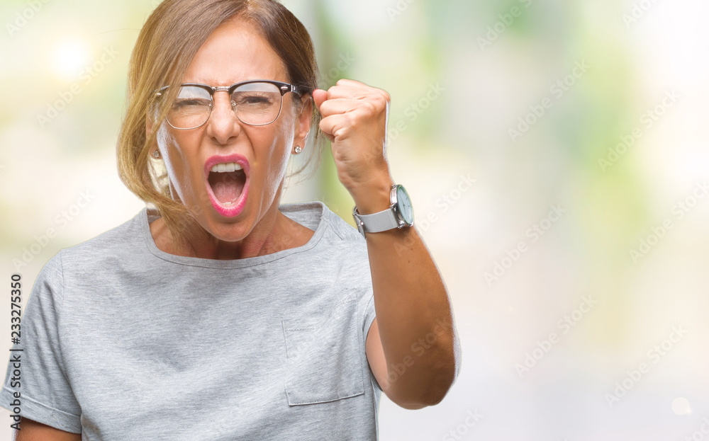 Middle age senior hispanic woman wearing glasses over isolated background angry and mad raising fist frustrated and furious while shouting with anger. Rage and aggressive concept.