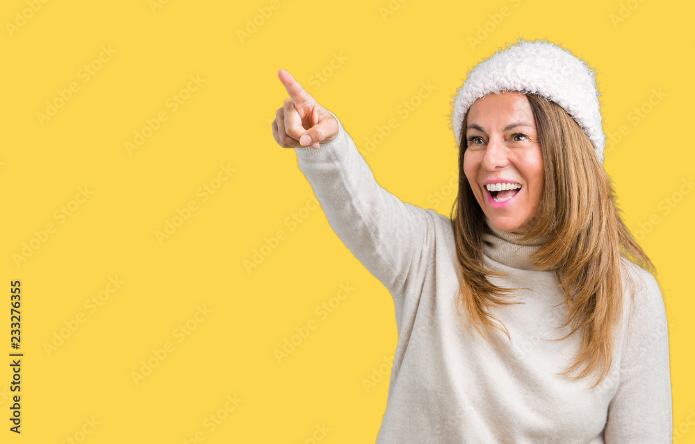 Beautiful middle age woman wearing winter sweater and hat over isolated background Pointing with finger surprised ahead, open mouth amazed expression, something in front Beautiful middle age woman wearing winter sweater and hat over isolated background Pointing with finger surprised ahead, open mouth amazed expression, something in front