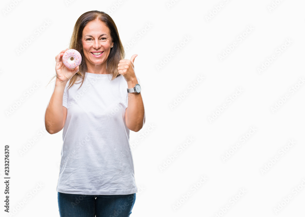 Middle age hispanic woman eating pink donut over isolated background pointing and showing with thumb up to the side with happy face smiling Middle age hispanic woman eating pink donut over isolated background pointing and showing with thumb up to the side with happy face smiling