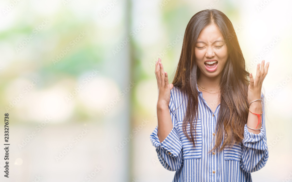 Young asian woman over isolated background celebrating mad and crazy for success with arms raised and closed eyes screaming excited. Winner concept Young asian woman over isolated background celebrating mad and crazy for success with arms raised and closed eyes screaming excited. Winner concept