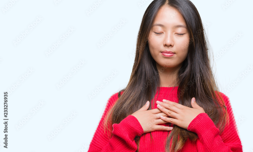 Young asian woman wearing winter sweater over isolated background smiling with hands on chest with closed eyes and grateful gesture on face. Health concept. Young asian woman wearing winter sweater over isolated background smiling with hands on chest with closed eyes and grateful gesture on face. Health concept.