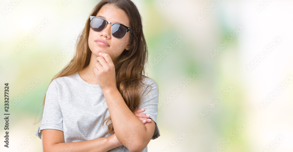 Young beautiful brunette woman wearing sunglasses over isolated background with hand on chin thinking about question, pensive expression. Smiling with thoughtful face. Doubt concept. Young beautiful brunette woman wearing sunglasses over isolated background with hand on chin thinking about question, pensive expression. Smiling with thoughtful face. Doubt concept.