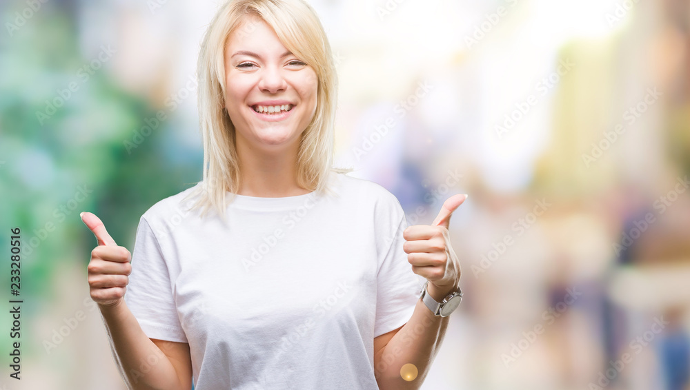 Young beautiful blonde woman wearing white t-shirt over isolated background success sign doing positive gesture with hand, thumbs up smiling and happy. Looking at the camera with cheerful expression