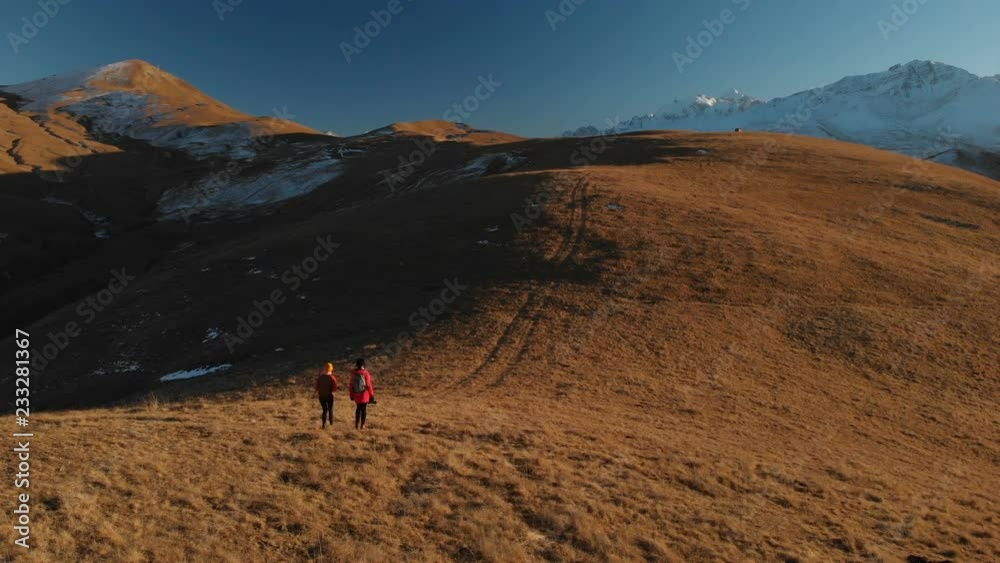 Aerial view of a two girls traveler with backpacks and cameras stroll through the hills between the epic rocks in the mountains. Girls photographers with their cameras at sunset Aerial view of a two girls traveler with backpacks and cameras stroll through the hills between the epic rocks in the mountains. Girls photographers with their cameras at sunset