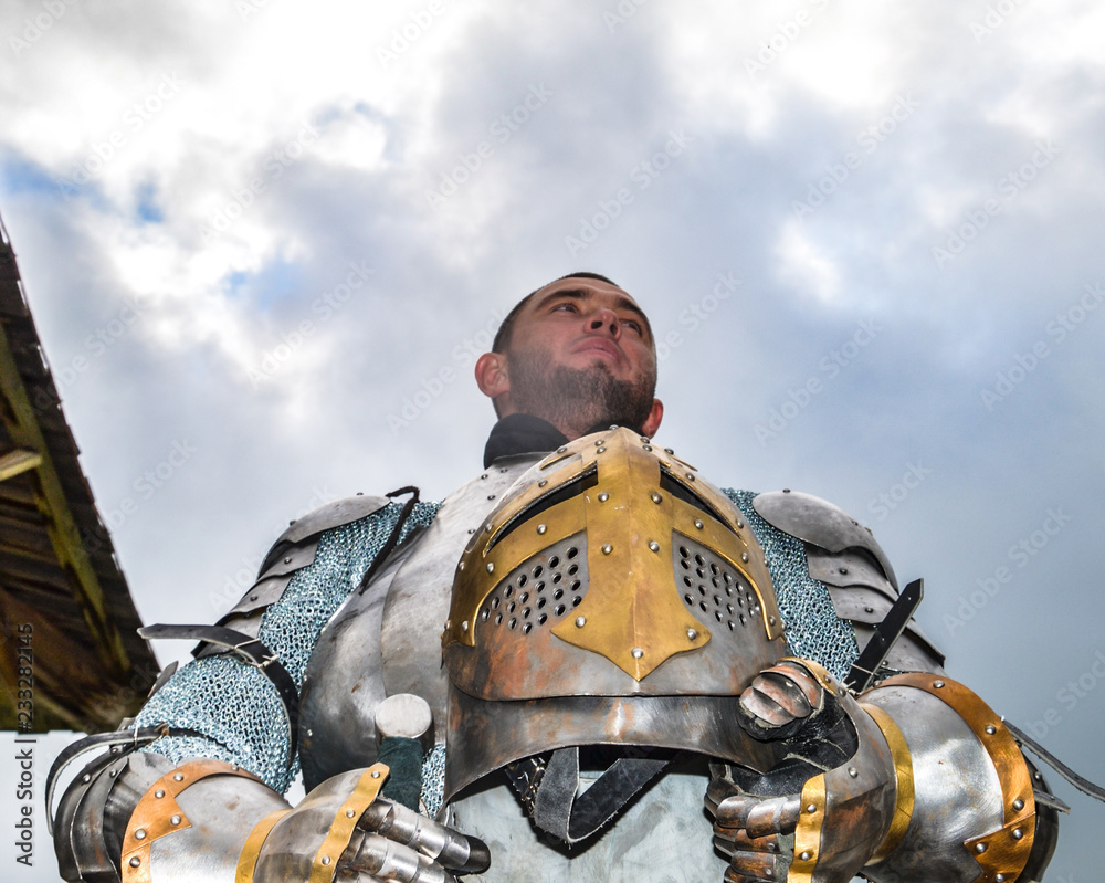Naklejka premium Knight in armor on the background of a cloudy sky. Knightly armor and weapon. Semi - antique photo.