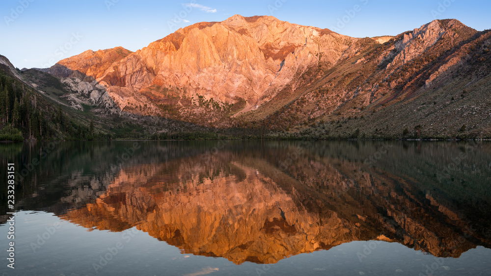 Panorama of the golden light of sunrise on mountain peaks reflected in the calm waters of Convict Lake in the eastern Sierra Nevada mountains of California