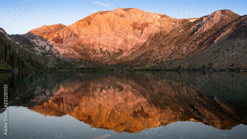 Panorama of the golden light of sunrise on mountain peaks reflected in the calm waters of Convict Lake in the eastern Sierra Nevada mountains of California