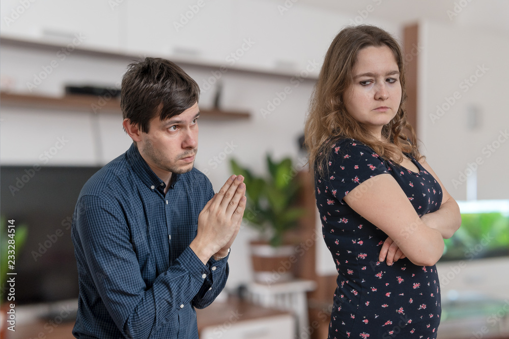 Fototapeta premium Young man is begging for forgiveness young angry woman at home.