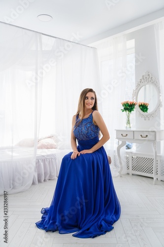 A beautiful girl in a blue long dress posing in a bright Studio.