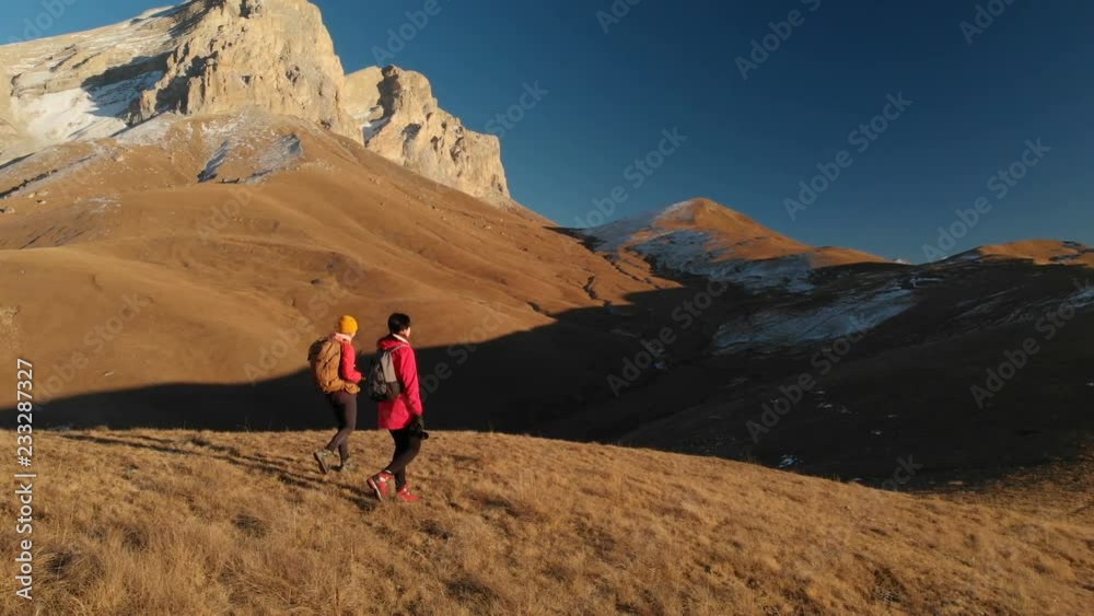 Aerial view of a two girls traveler with backpacks and cameras stroll through the hills between the epic rocks in the mountains. Girls photographers with their cameras at sunset Aerial view of a two girls traveler with backpacks and cameras stroll through the hills between the epic rocks in the mountains. Girls photographers with their cameras at sunset