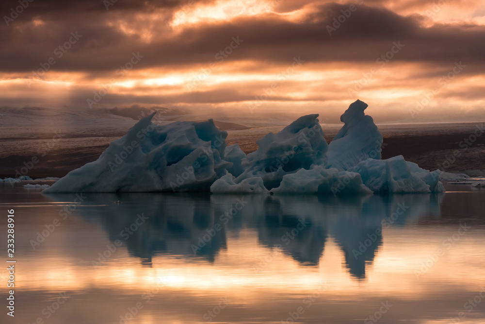 The Jökulsárlón is a large glacial lake in southeast Iceland, the floating ice floes on a quiet surface of gracial lagoon, a dramatic sunset sky is reflected on the surface