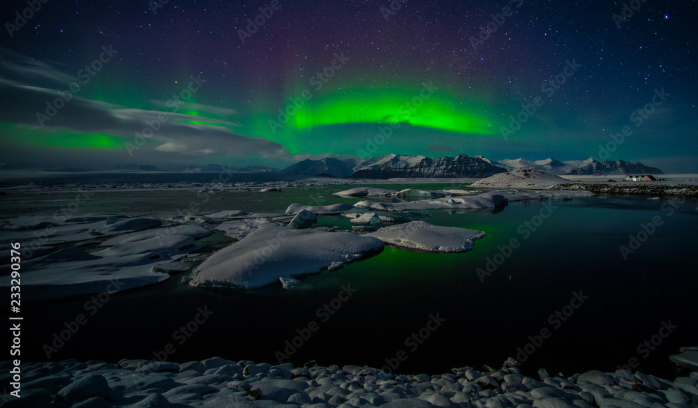 Fototapeta premium A beautiful green aurora borealis dancing over the Jokulsarlon lagoon, Iceland. In the forground is reflection in the lake surface. In the background are the northern lights above the mountains.
