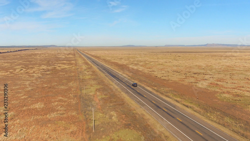 AERIAL: SUV car driving along a freight train on scenic countryside empty road