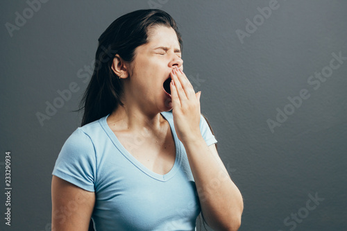 Young woman yawning. Studio portrait isolated on grey background.
