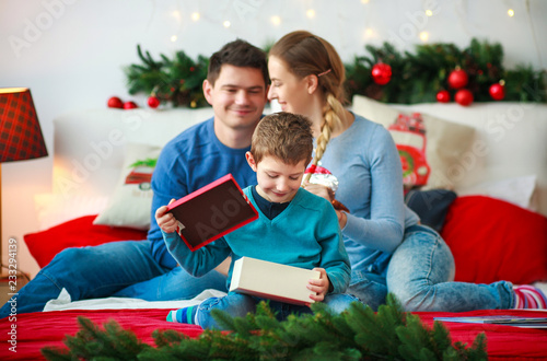 Joyful boy with parents opens New Year's gift box at Christmas home © okostia