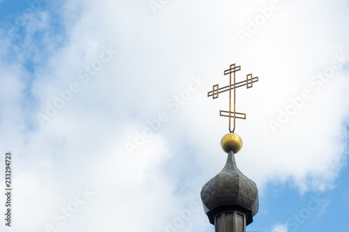 Orthodox cross close up on the tower of the middle church in the background of blue sky and clouds. The concept of Christianity, the symbol of the Orthodox faith in God