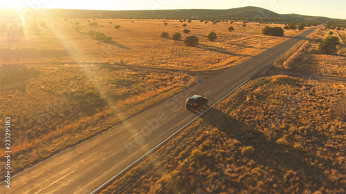 Canvastavla AERIAL: Black SUV car driving along empty country road at golden summer sunset